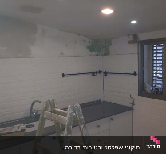 סולם עץ עם כתמי צבע ליד קיר צבוע חלקית